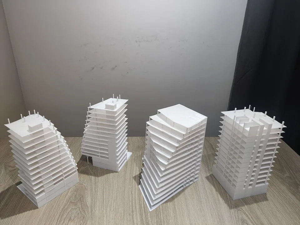 Four white 3D printed high-rise building models on a wooden table, with thin flat floor slabs projecting beyond columns