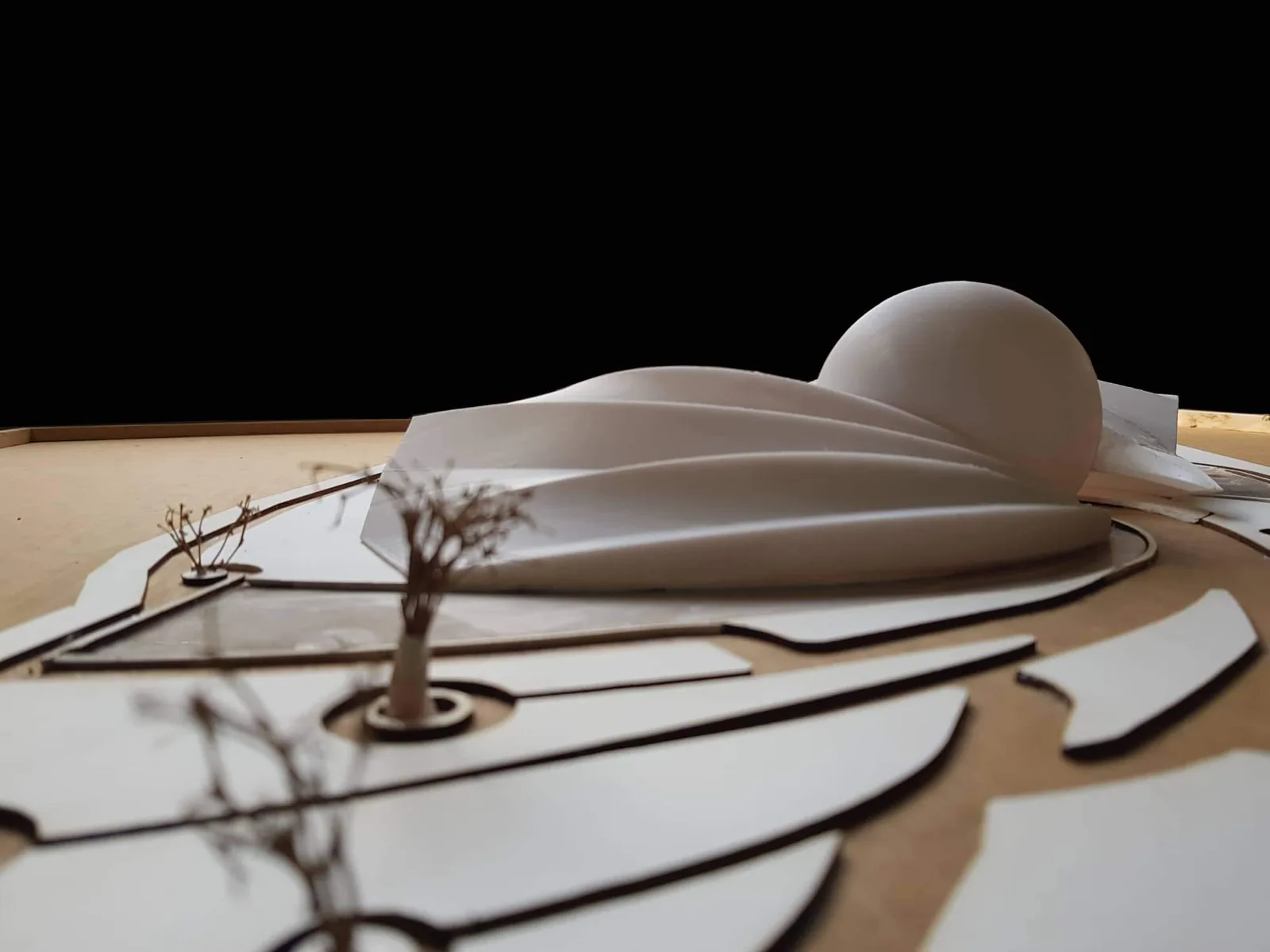 Low side view of a white 3D-printed theatre model with layered curved roofs and a large dome on a site board